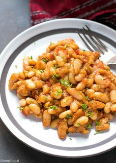 a white plate topped with beans covered in sauce and garnished with parsley