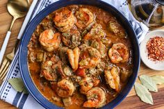 a blue bowl filled with shrimp and vegetables on top of a wooden table next to silverware