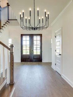 an empty room with a chandelier and wooden stairs leading up to the front door