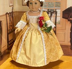 a doll is dressed in a yellow dress with white lace on the top and red roses at the bottom