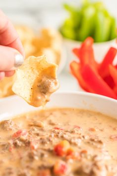 a person dipping tortilla chips into a bowl of quesadilla soup