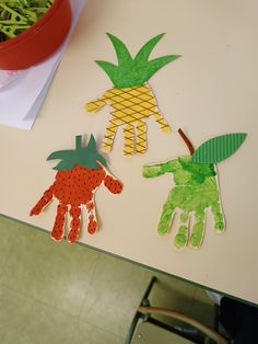 three handprints made to look like fruits and vegetables on a table next to a potted plant