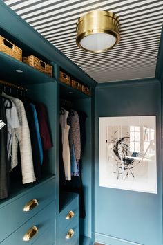 a blue closet with clothes hanging on the wall and a gold light fixture above it