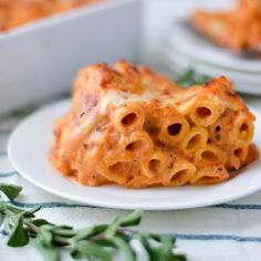 a white plate topped with cheesy pasta covered in sauce and garnished with green leaves