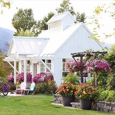 a white house with lots of flowers in the front yard and patio area next to it