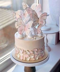 a three tiered cake with pink butterflies on it sitting in front of a window