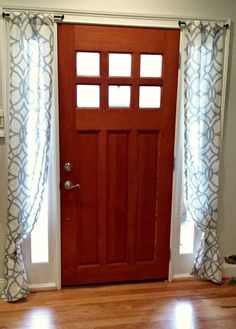 a red door with white curtains and a cat sitting on the floor in front of it