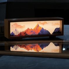 an illuminated box with a mountain scene on the front and reflection in the water behind it