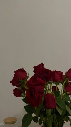 a vase filled with red roses sitting on top of a table next to a white wall