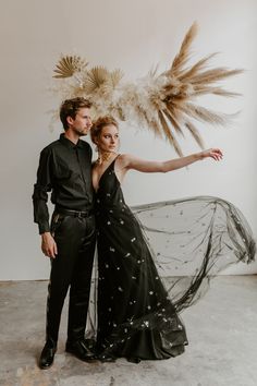 a man and woman posing for a photo in front of a wall with feathers on it