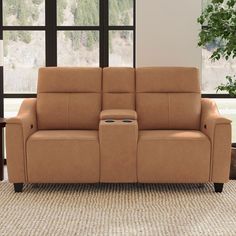 a tan leather reclining sofa with two seats in front of a large window and potted plant