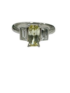 This platinum diamond trilogy ring weighs 5.2 grams. Nice and sturdy, the ring is made up of a center elongated radiant cut diamond, eye clean and fancy yellow in color, and securely set in a four pronged setting. The diamond has a beautiful elongated shape, measuring 7.8x3.9 mm and weighs 0.71 carats (stamped). It has been jeweler graded to be fancy light yellow in color and VS1 in clarity with lots of brilliance and life. A very fiery yellow diamond. It is flanked by a pair of baguette cut diamonds, combining to weigh 0.60 carats (stamped). They have been jeweler graded to be E-F in color and VS1 in clarity. The ring's head rises 5.0 mm off the finger and the ring comes as a size 5.75; it can easily be resized to half a size for free. Elongated Radiant Cut, Elongated Radiant, Diamond Trilogy Ring, Fancy Light, Diamond Baguette, Trilogy Ring, Fancy Lights, Radiant Cut Diamond, Radiant Diamond