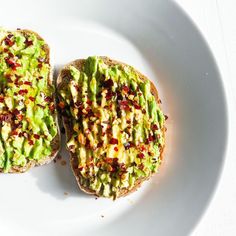 two pieces of toast with avocado and other toppings on it sitting on a white plate