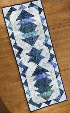 a blue and white table runner on top of a wooden floor next to a vase