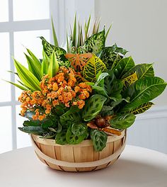 a basket filled with lots of green and orange flowers on top of a white table