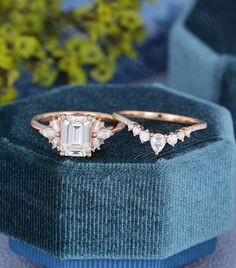 two wedding rings with diamonds on top of a blue velvet box next to some flowers