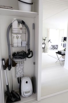 a white closet filled with different types of cleaning supplies and accessories on shelves next to a doorway