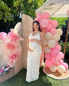 a pregnant woman standing in front of a giant balloon arch with pink and white balloons