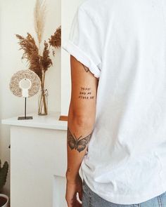 a man with a butterfly tattoo on his left arm and right arm is standing in front of a white wall