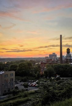 the sun is setting over an urban area with tall buildings and trees in the foreground