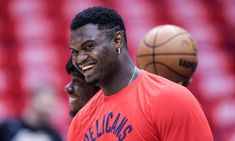 two basketball players are smiling while standing in front of a ball on the court and one is wearing an orange t - shirt