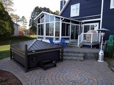 a patio with a hot tub in front of a large blue house on a sunny day