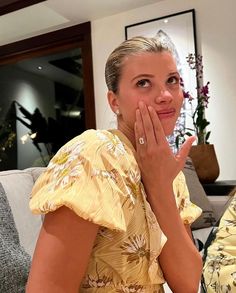 a woman sitting on a couch with her hand to her face and looking at the camera