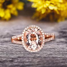 an oval shaped peach morganite surrounded by diamonds on a wooden surface with yellow flowers in the background