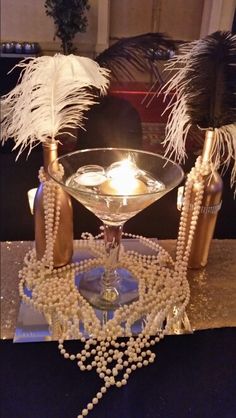 a table topped with a martini glass filled with liquid and pearls next to two candles