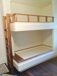 a white bunk bed sitting in a bedroom next to a wooden ladder and wall mounted shelf