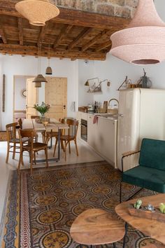 a living room and dining area in an old house with exposed wood beams, wooden table, green chair, white refrigerator and brick ceiling