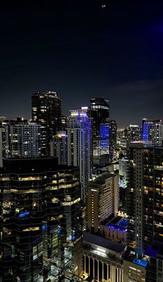 the city skyline is lit up at night with bright lights and skyscrapers in the foreground