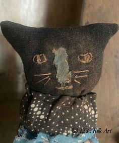 a black cat stuffed animal sitting on top of a blue polka dot cloth pillow with holes in the fabric