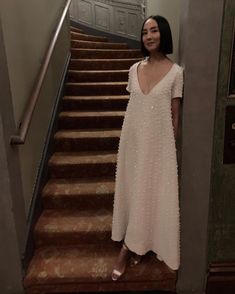 a woman in a white dress standing at the bottom of stairs