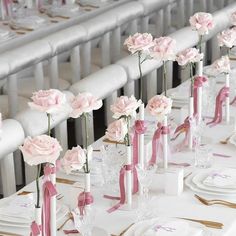 there are many pink flowers in vases on the table with white plates and place settings