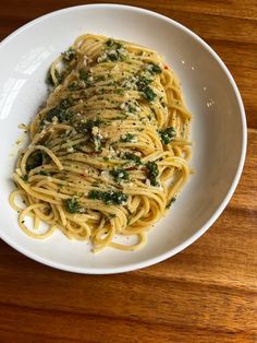 a white bowl filled with pasta covered in pesto and parmesan on top of a wooden table