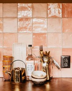 kitchen counter with utensils, wine bottle and other items on it in front of pink tiled wall