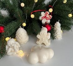 some white candles sitting on top of a table next to christmas decorations and lights in front of a tree