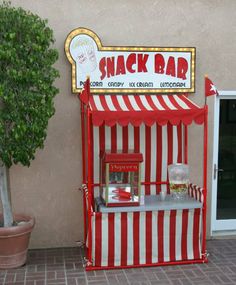 a red and white striped stand next to a potted plant on the side of a building