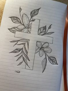 a drawing of a cross with leaves and flowers on it, sitting on top of a notebook