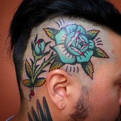 a man with a tattoo on his head has a blue flower and leaves behind it