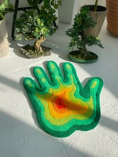 a green and yellow hand rug sitting on top of a white floor next to potted plants