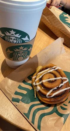 a cinnamon roll sitting on top of a table next to a cup of starbucks coffee