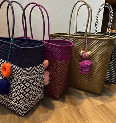 four woven bags with tassels and pom poms are lined up on the floor