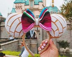 a hand holding up a minnie mouse ears headband in front of a castle at disneyland