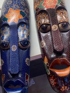 two wooden masks with painted designs on them sitting next to each other in front of a wall