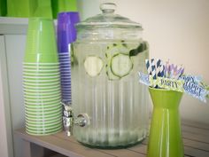 there are many different colored vases on the shelf next to each other, including one with cucumbers in it