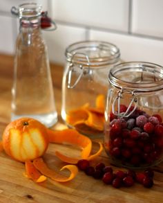 three glass jars filled with fruit sitting on top of a wooden table next to orange slices