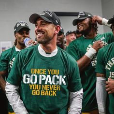 a group of men standing next to each other wearing green and white shirts with the words go pack you never go back on them