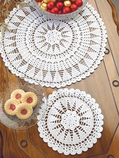 two crocheted doily on top of a wooden table next to a bowl of fruit